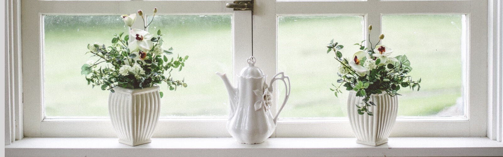 two flowerpoints on a sunny windowsill with a kettle in between